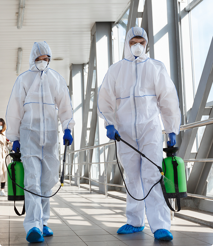 Two male commercial cleaners in white coverall suits and masks with commercial-grade disinfectants in hand.