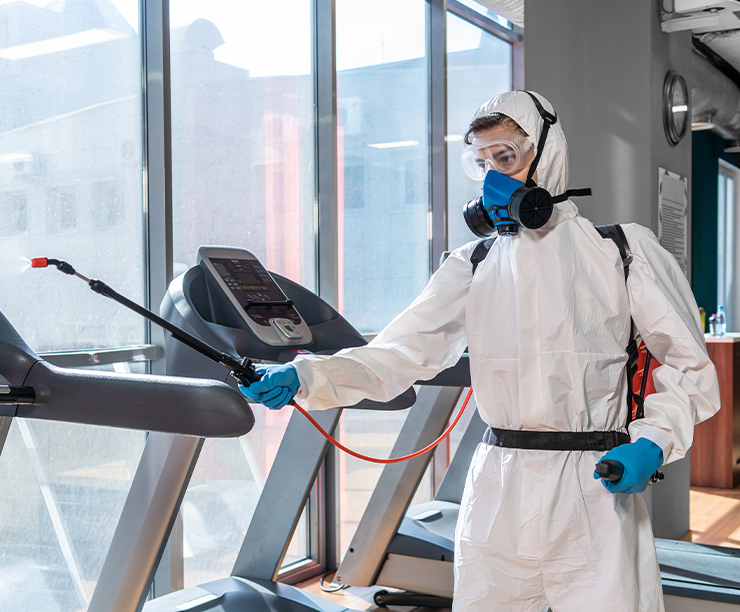 Commercial cleaner in white coveralls wiping the arm of a treadmill at a Oklahoma City fitness center.